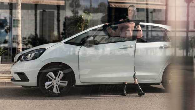 Zijaanzicht van Honda Jazz geparkeerd met dame die het portier opent