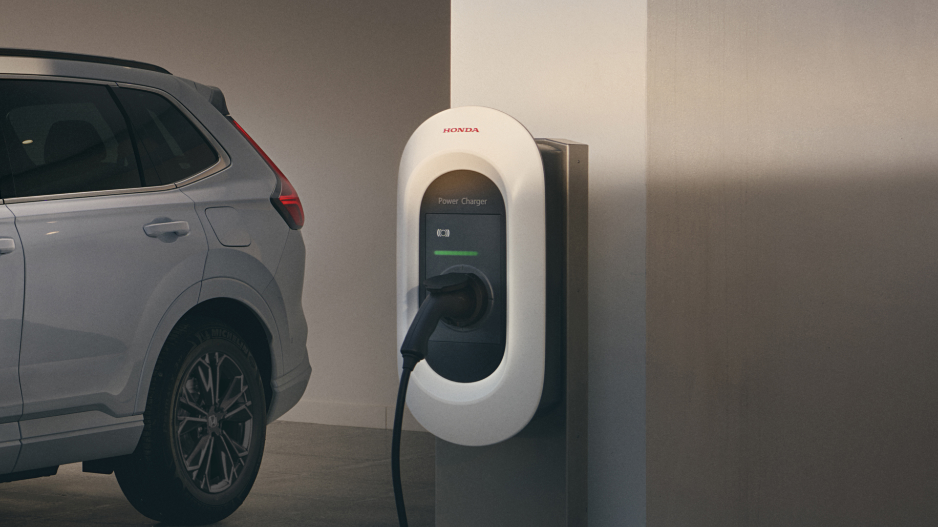 Driekwart vooraanzicht van de Honda CR-V Hybride ingeplugd op laadstation.