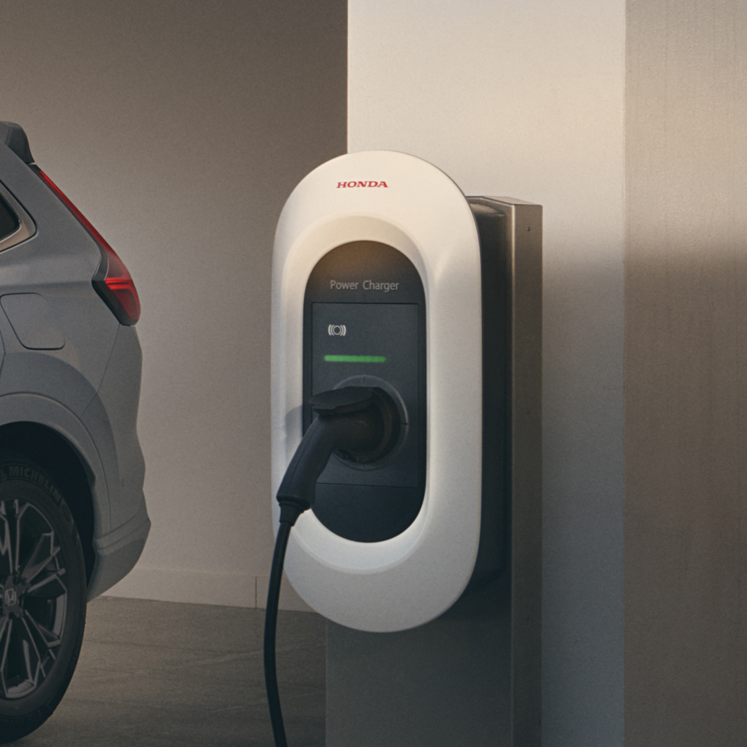 Driekwart vooraanzicht van de Honda CR-V Hybride ingeplugd op laadstation.