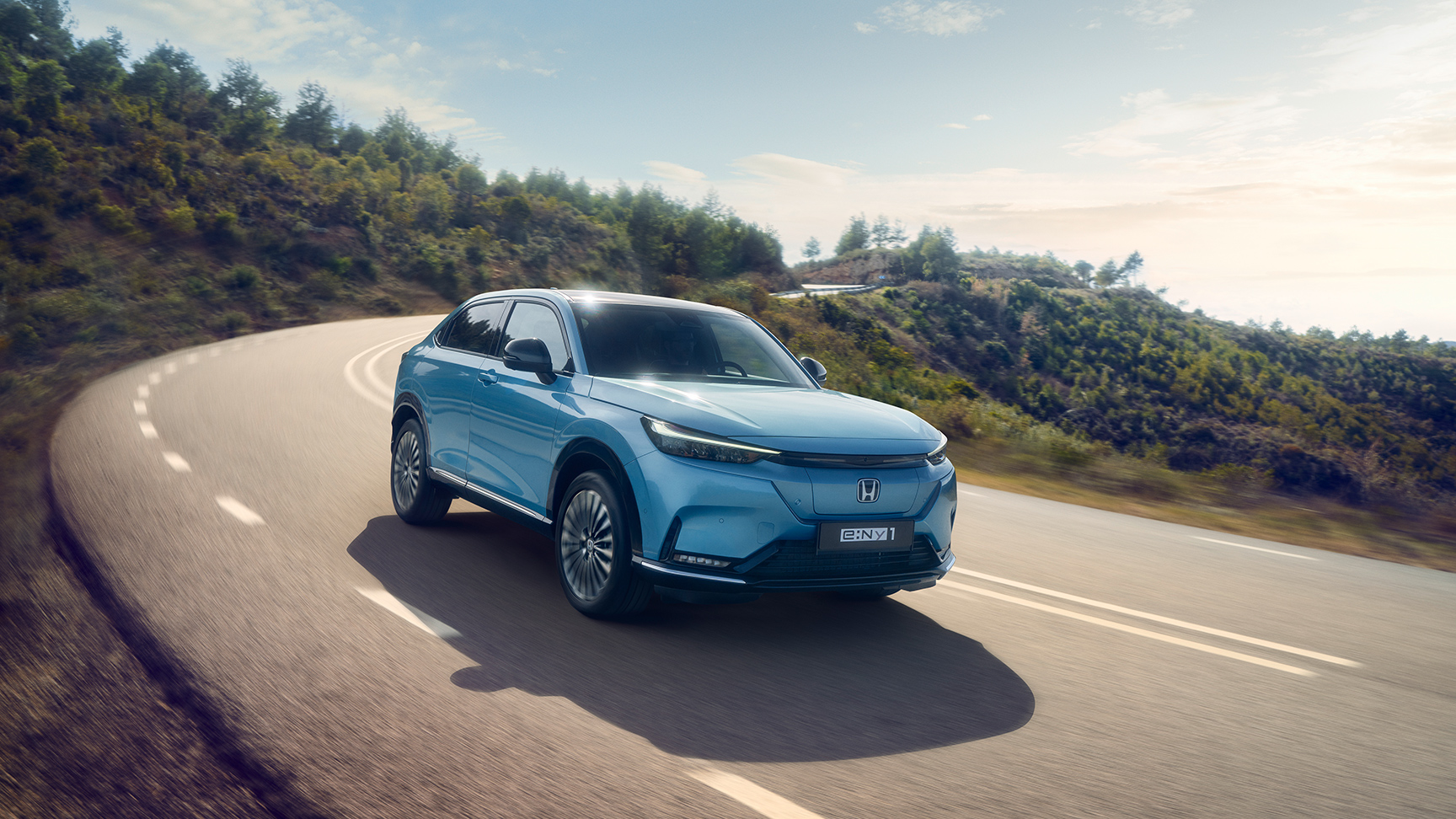 Vooraanzicht Honda e:Ny1 die rijdt over de weg in een landelijke omgeving.