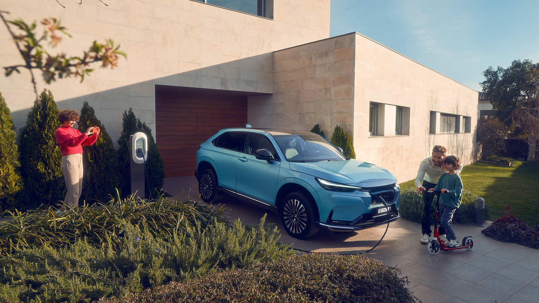 Gezin speelt op oprit naast Honda e:Ny1 die aan het opladen is op de oprit.