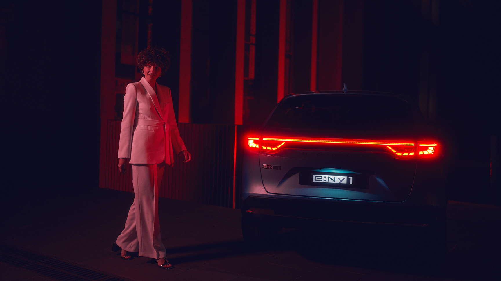 Model naast de verlichte achterkant van de Honda e:Ny1 bij nacht.