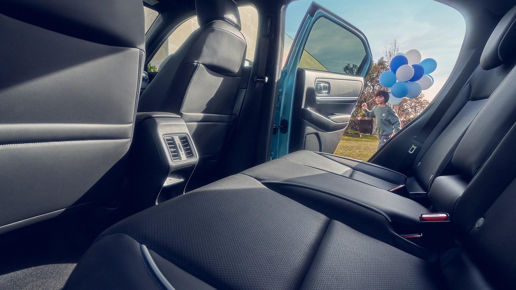 Close-up van de achterzetel in de Honda e:Ny1 met een kind met ballonnen dat langs de openstaande deur loopt.