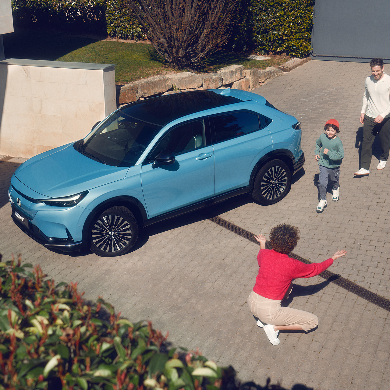 Familie rondom een geparkeerde Honda e:Ny1 op een oprit.