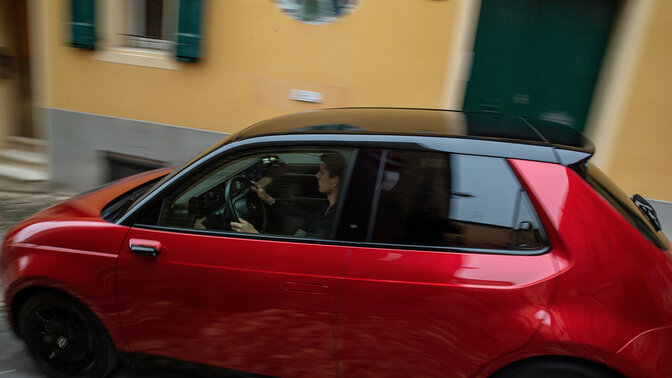Driekwart vooraanzicht Honda e, 's nachts rijdend in een elektrisch stadslandschap.