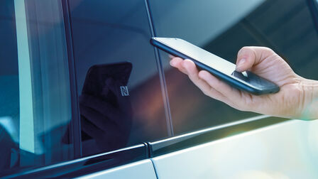 Persoon met een smartphone bij de deur van een Honda e. 