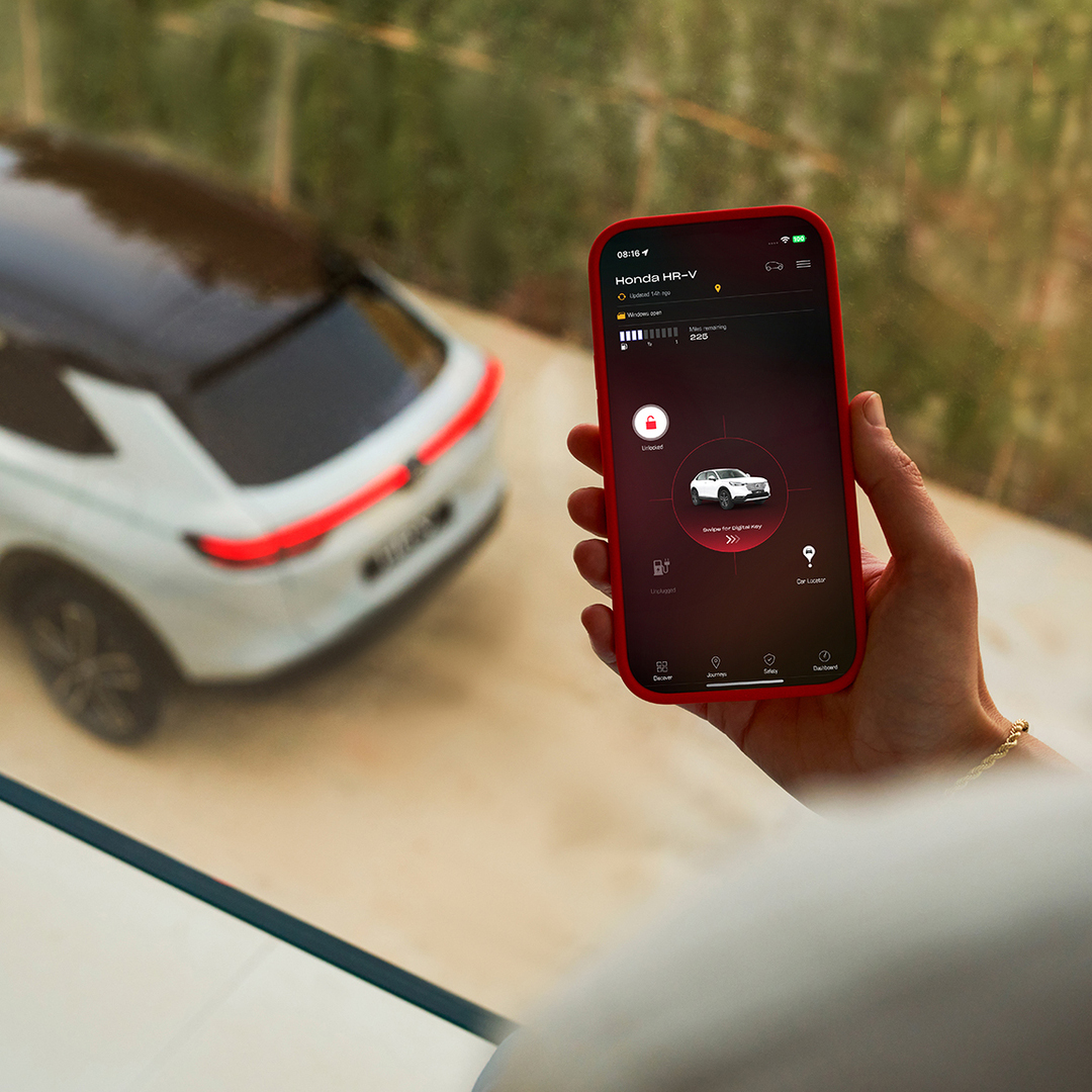A person holds a smartphone displaying a vehicle charging settings app while a white SUV is parked in the background.