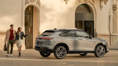 Zijaanzicht van de Honda HR-V buiten een hotellocatie, met een koppel dat langsloopt. 