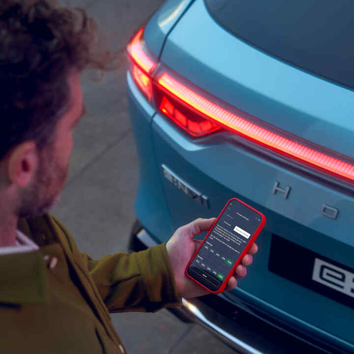 My Honda+ app close-up van persoon met telefoon naast een auto