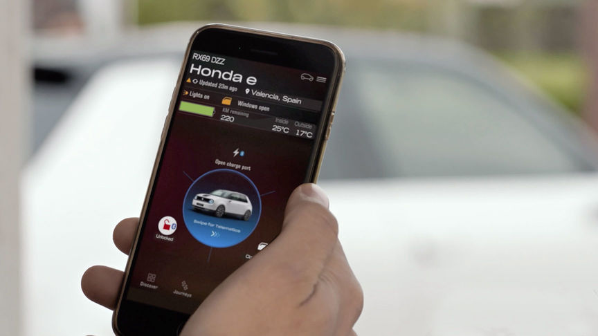 Een man kijkt naar de My Honda+ app met een Honda Jazz Hybrid Crosstar op de achtergrond. 