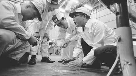 Soichiro Honda en enkele fabrieksmedewerkers in witte overalls.