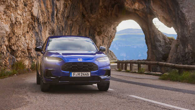De ZR-V Hybrid SUV met blauwe sportieve aandrijflijn, op weg in een bergachtige omgeving.