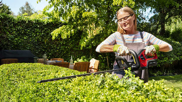 Vrouw trimt heg met accu Honda heggenschaar in een tuin.