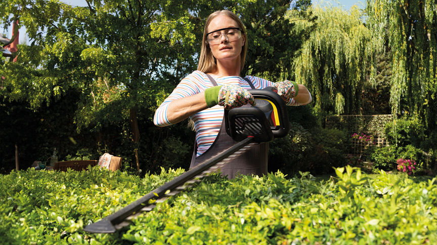 Vrouw gebruikt accu Honda heggenschaar om haag in tuin te snoeien.
