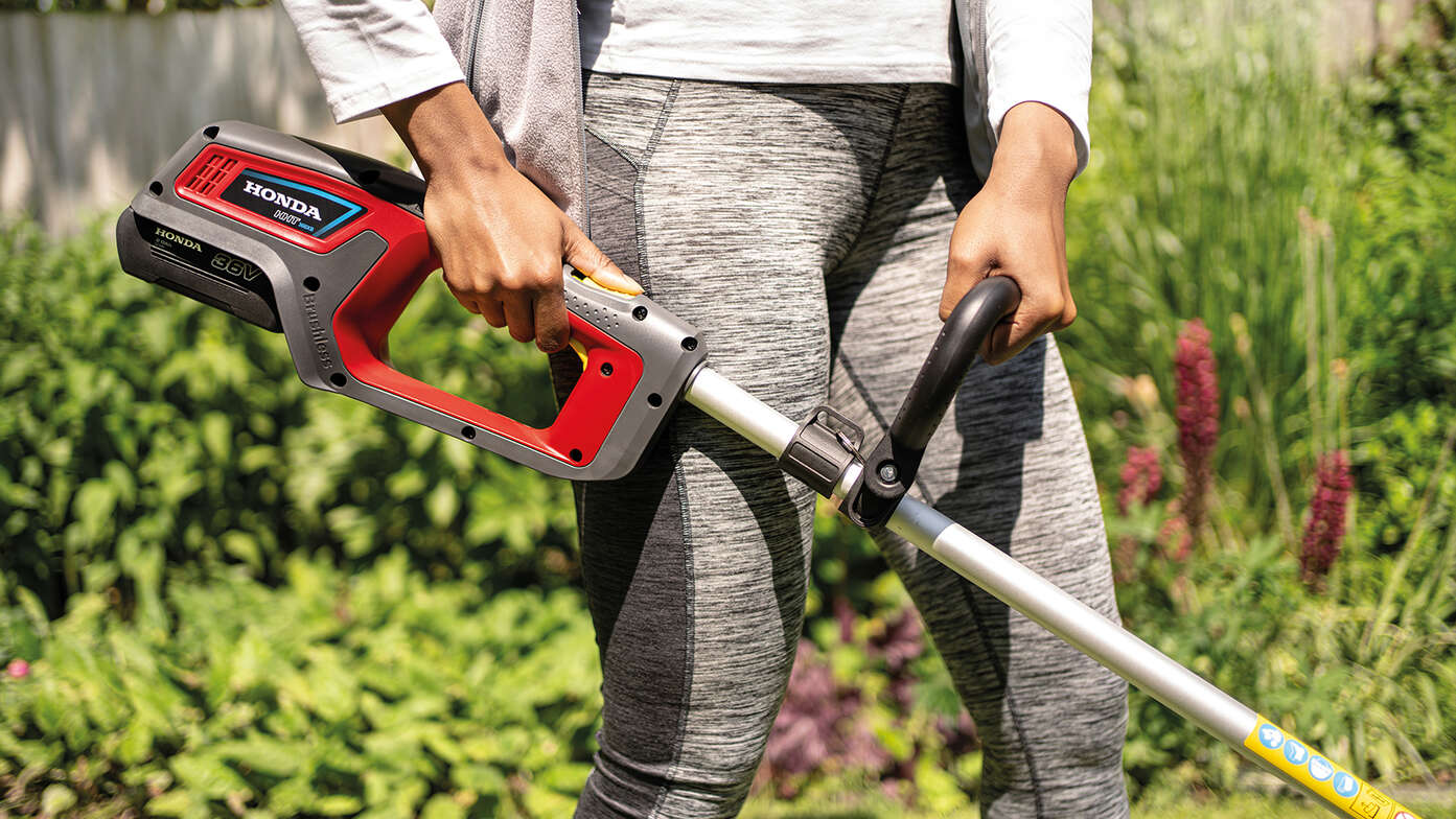 Close-up van vrouw die Honda accu grastrimmer in de tuin gebruikt.