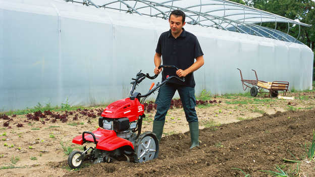 Vooraanzicht roterende tuinfrees aan het werk op het land. 