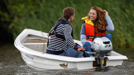 A couple smiling, in a boat on a lake.