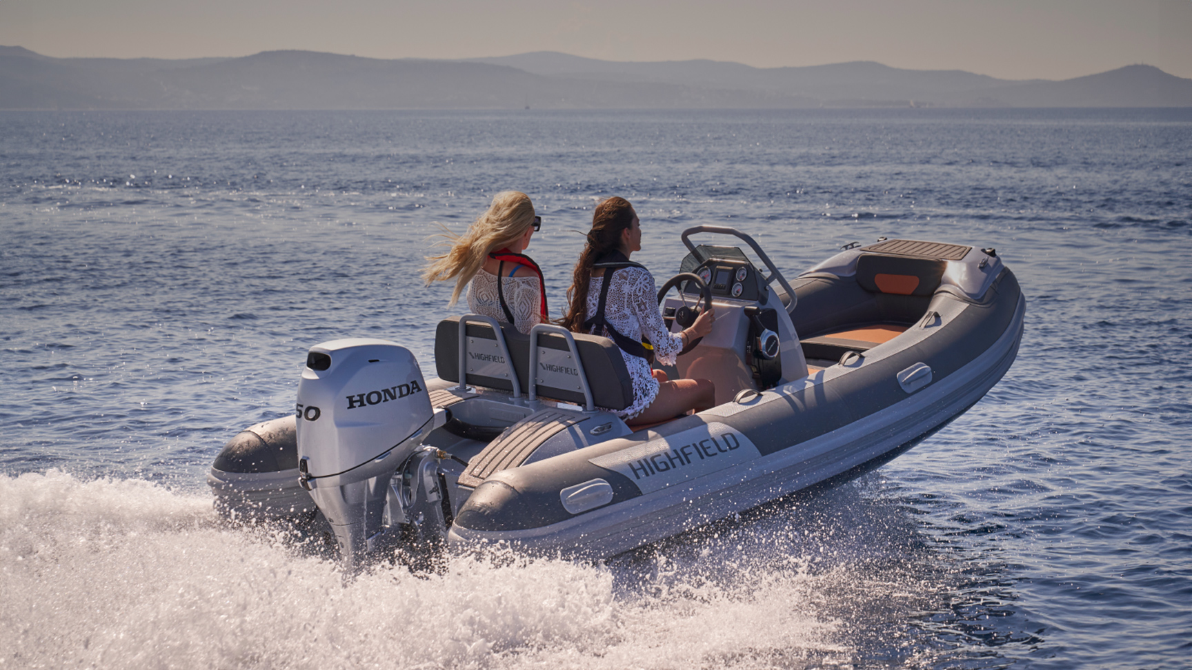 Twee modellen op een Highfield-boot met Honda BF50-motor op een locatie aan zee.