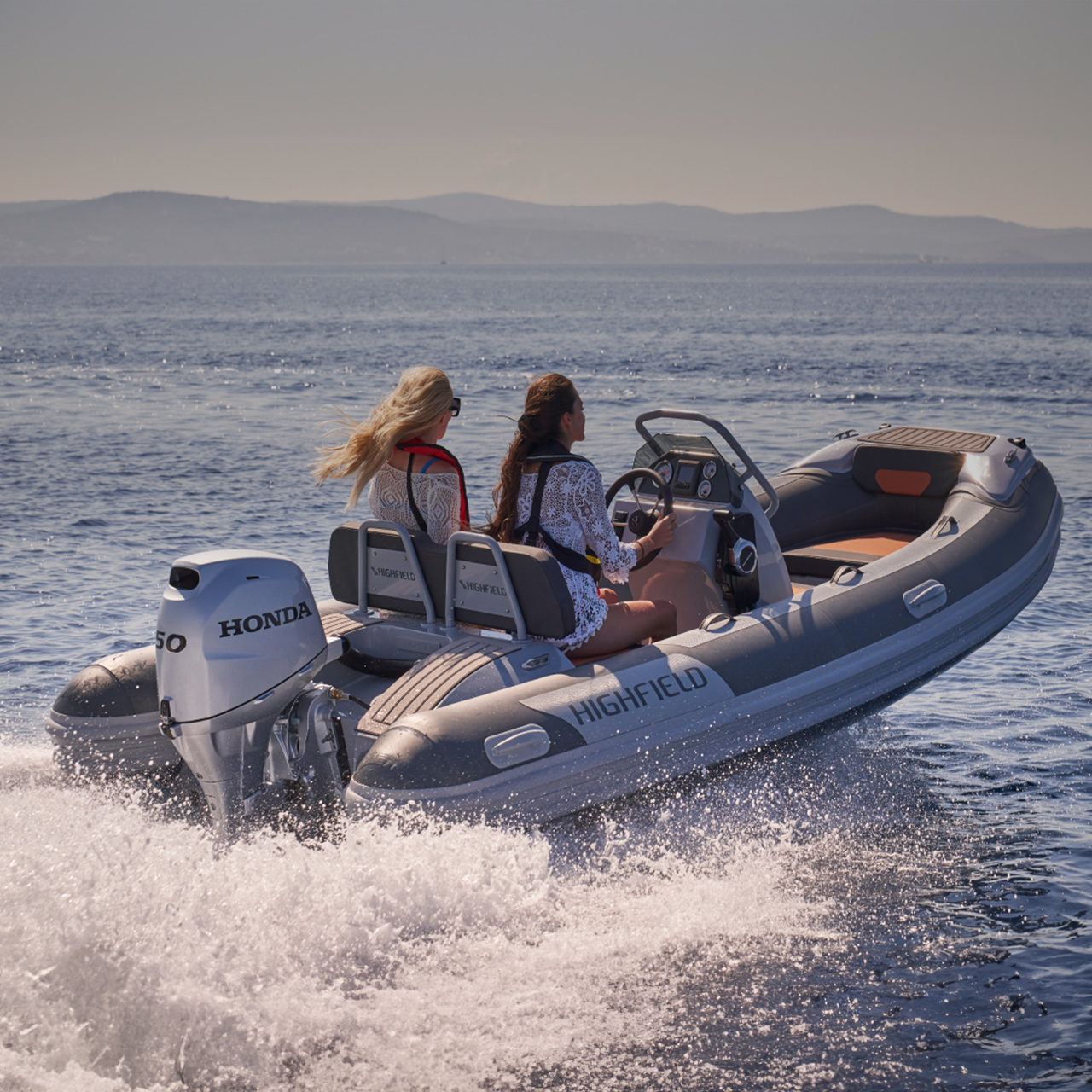 Twee modellen op een Highfield-boot met Honda BF50-motor op een locatie aan zee.