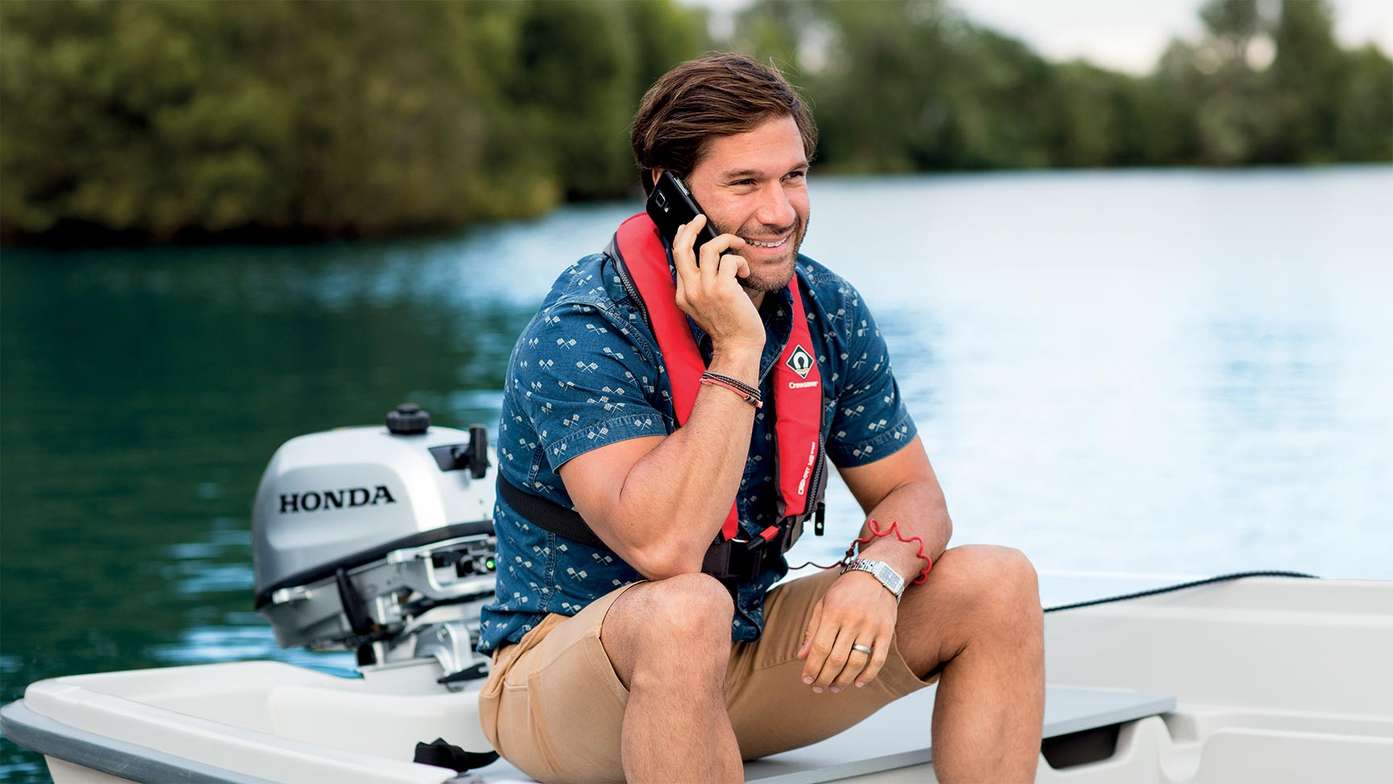 Man on small boat charging his phone off of his Honda Outboard engine while talking
