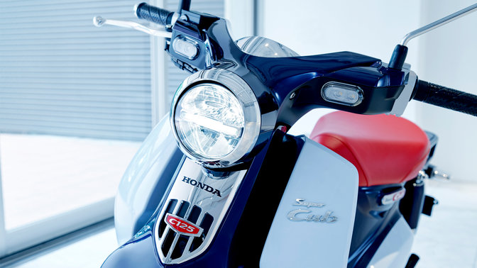 Honda Super Cub, geparkeerd op een moderne locatie.