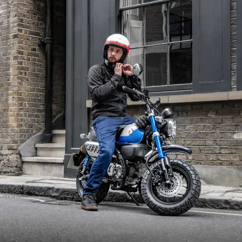 Honda Monkey 125 met rijder geparkeerd langs de baan