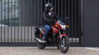 Driekwarts vooraanzicht, rechterzijde van rode CB125F, rijder op de motorfiets stilstaand, stedelijke omgeving