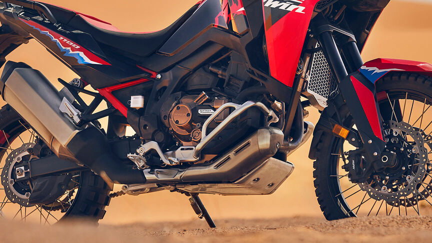 Model rijdend op een CRF1100L Africa Twin motorfiets op een woestijnlocatie.