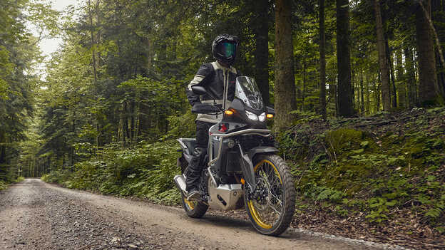Model rijdend op Honda XL750 Transalp in een bosomgeving.
