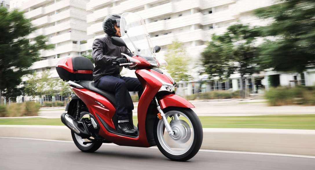 Honda SH125i, driekwart rechtervooraanzicht, met rijder in de stad