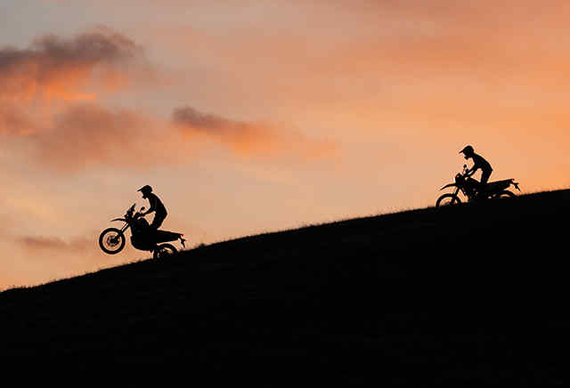 Twee Hondamotorfietsen uit het 300-gamma rijdend bergaf in zonsondergang.