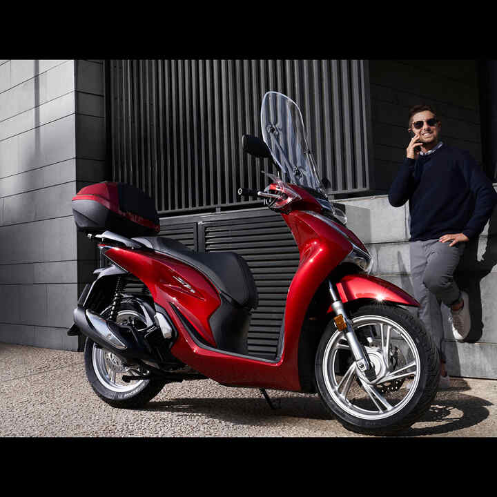 Man telefoneert naast Honda scooter.