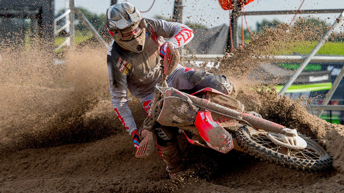 Vooraanzicht Honda off road motorfiets met rijder, glijdend door modder.