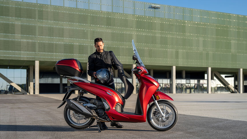 Honda SH350i driekwartvooraanzicht van rechts, met bestuurder, op de weg, rode motor