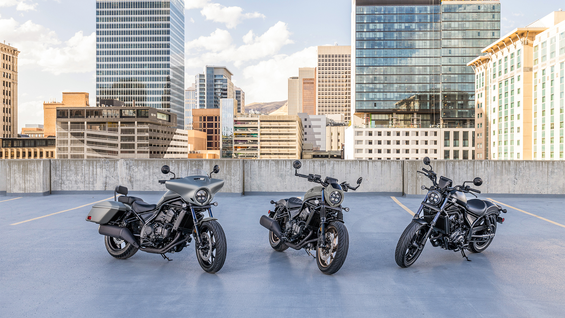 Drie CMX1100 motorfietsen buiten, voor moderne gebouwen.